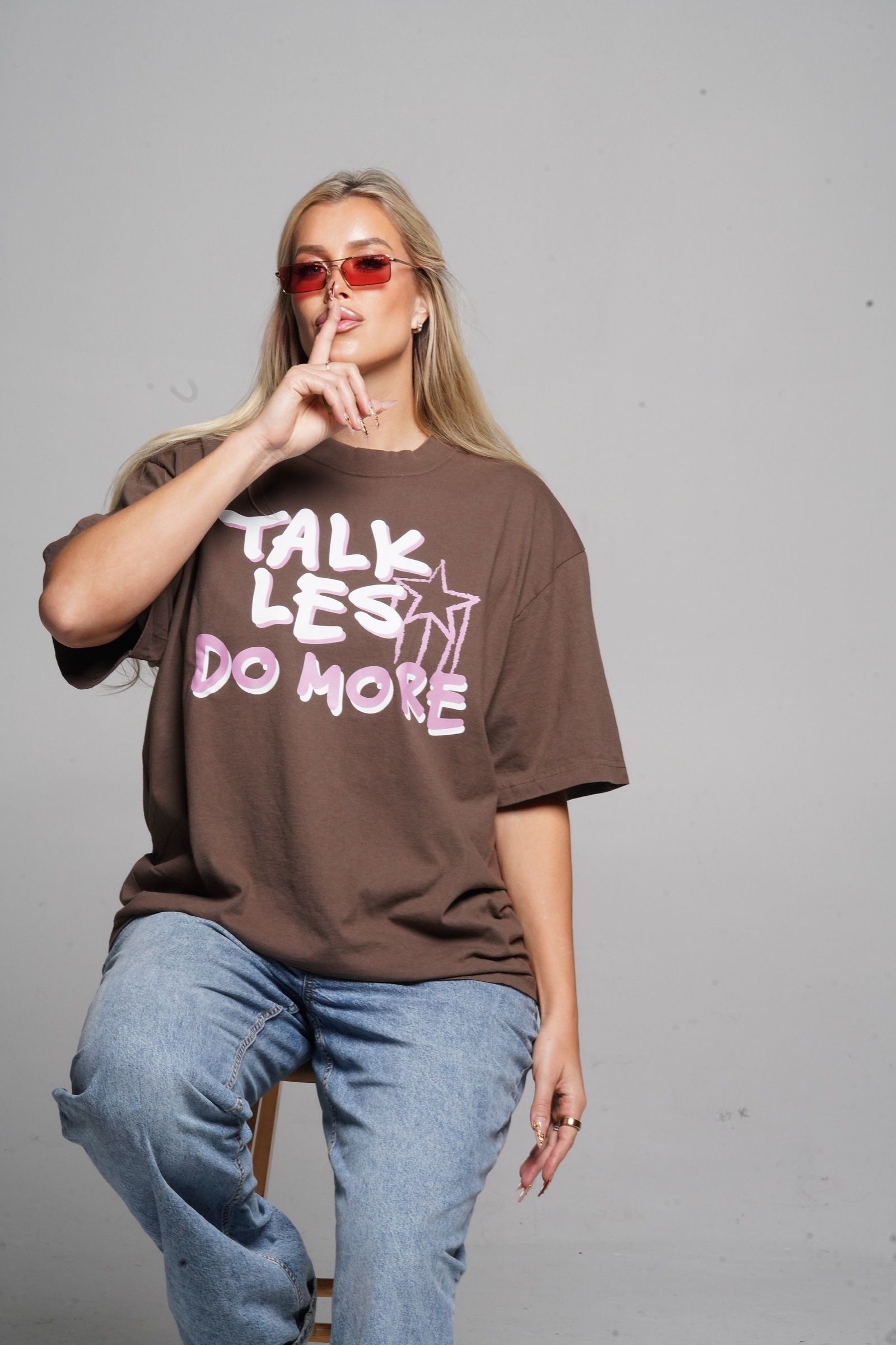 Les in the mocha Talk Les. Do More. tee and red sunglasses, finger to her lips